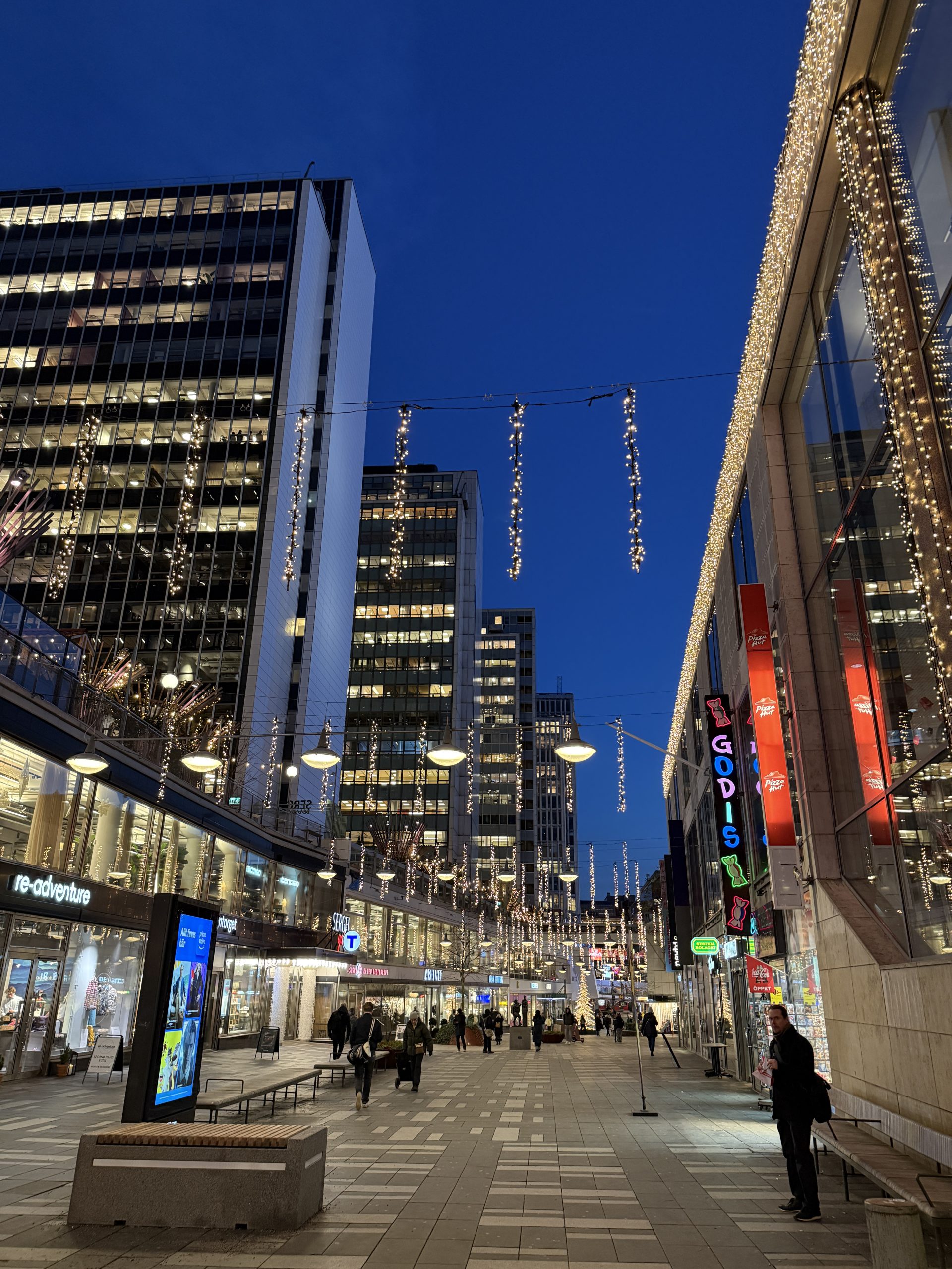 Sergelgatan i Stockholm under kvällstid med julbelysning och människor.