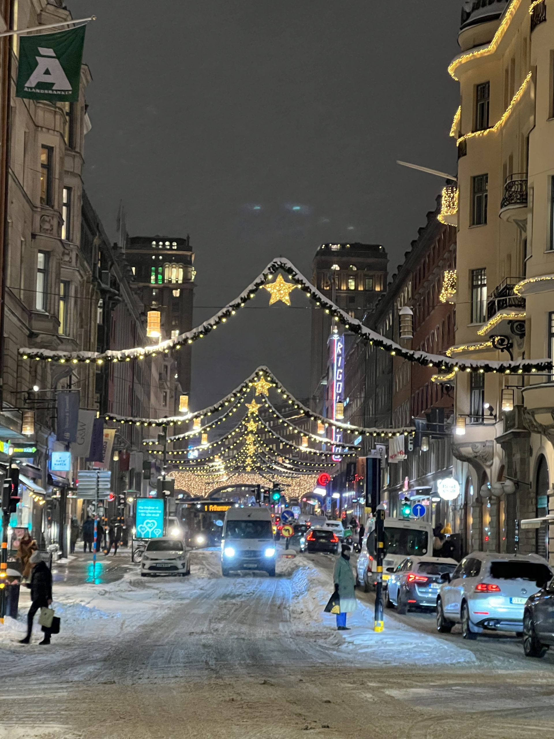 Snö på Kungsgatan i Stockholm med tänd julbelysning och trafik.