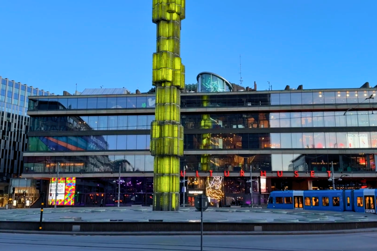Grön obelisk i Sergelfontänen i Stockholm. Blå himmel med Kulturhuset i bakgrunden.